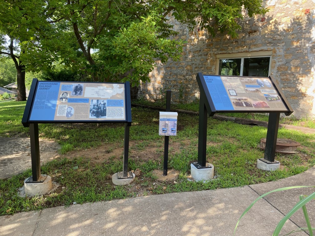 Two informational kiosks in front of the Grover Barn with a brochure holder between them.